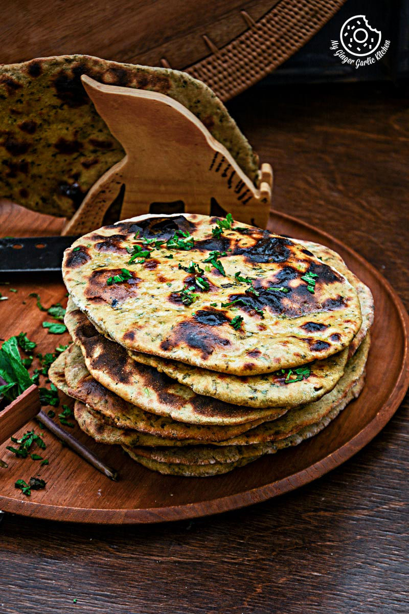 four mint coriander tandoori roti flatbreads on a wooden plate with mint leaves on the side