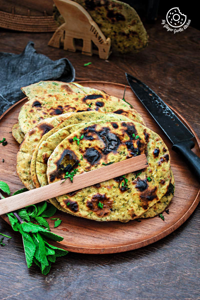 a few mint coriander tandoori roti flatbreads on a wooden plate with a tong