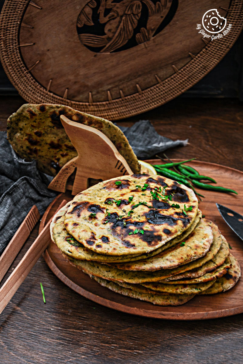 four mint coriander tandoori rotis on a plate with a tong and a bowl of green chillies