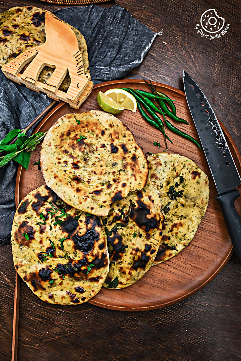 four mint coriander tandoori rotis on a wooden plate with a tong