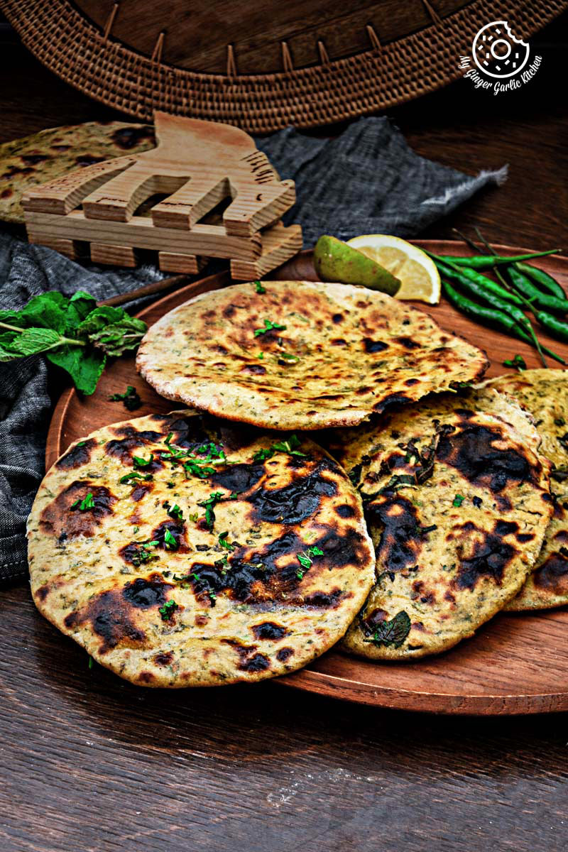 few mint coriander tandoori roti flatbreads on a wooden plate with a slice of lime and green chillies