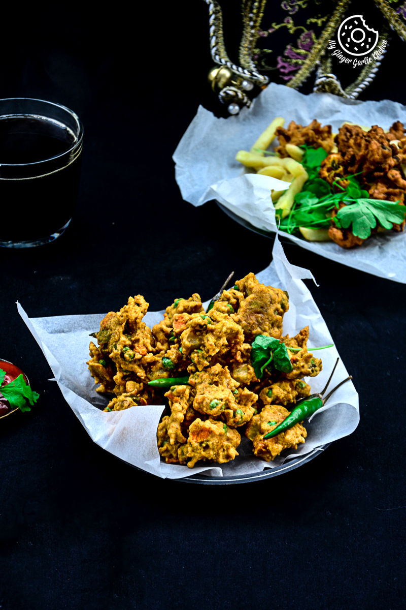 two plates of mix veg pakora on a table with a glass of beer