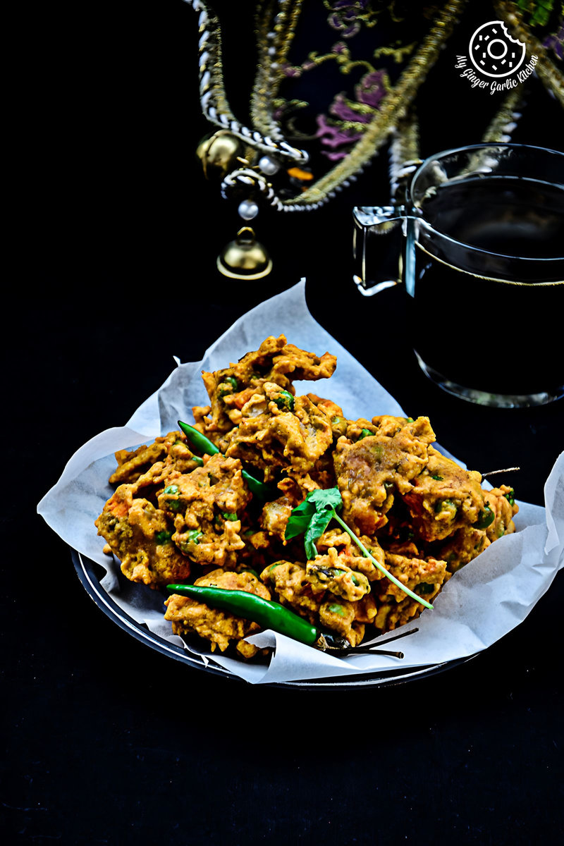 a plate of mix veg pakora on a table with a glass of tea