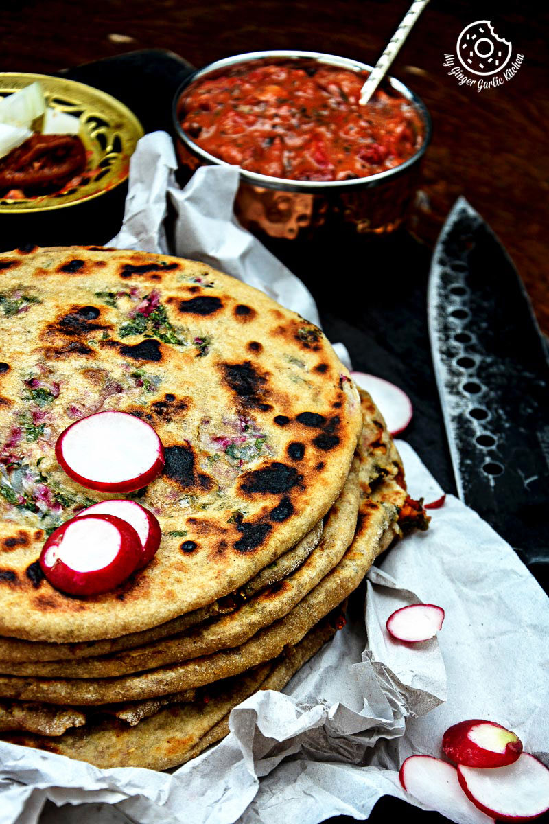 five mooli parathas stacked on a plate with radishes