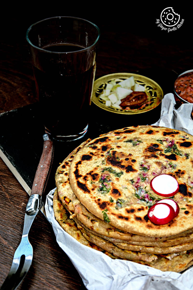 five mooli parathas stacked on a plate with a glass of soda