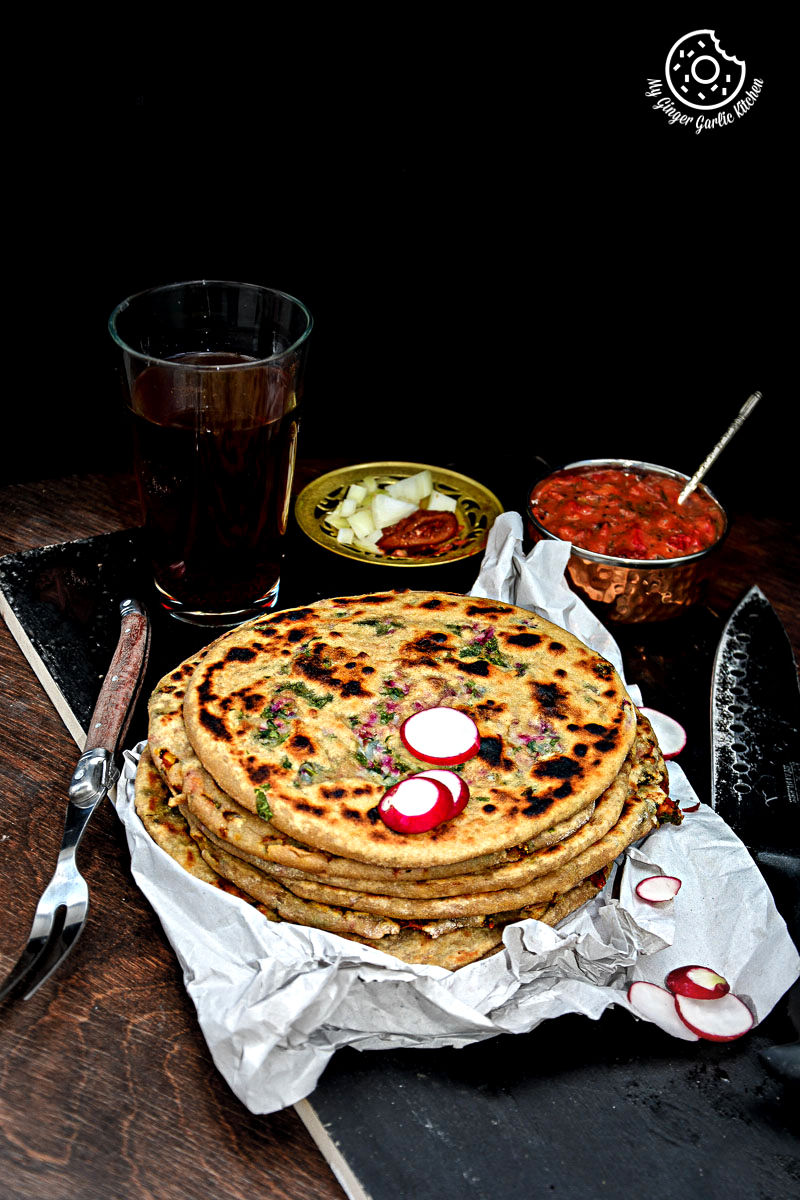 a stack of mooli paratha with strawberry grape chutney on a table with a glass of soda