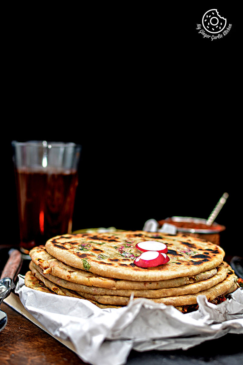 a stack of mooli paratha with strawberry grape chutney on a table with a glass of soda with a glass of soda