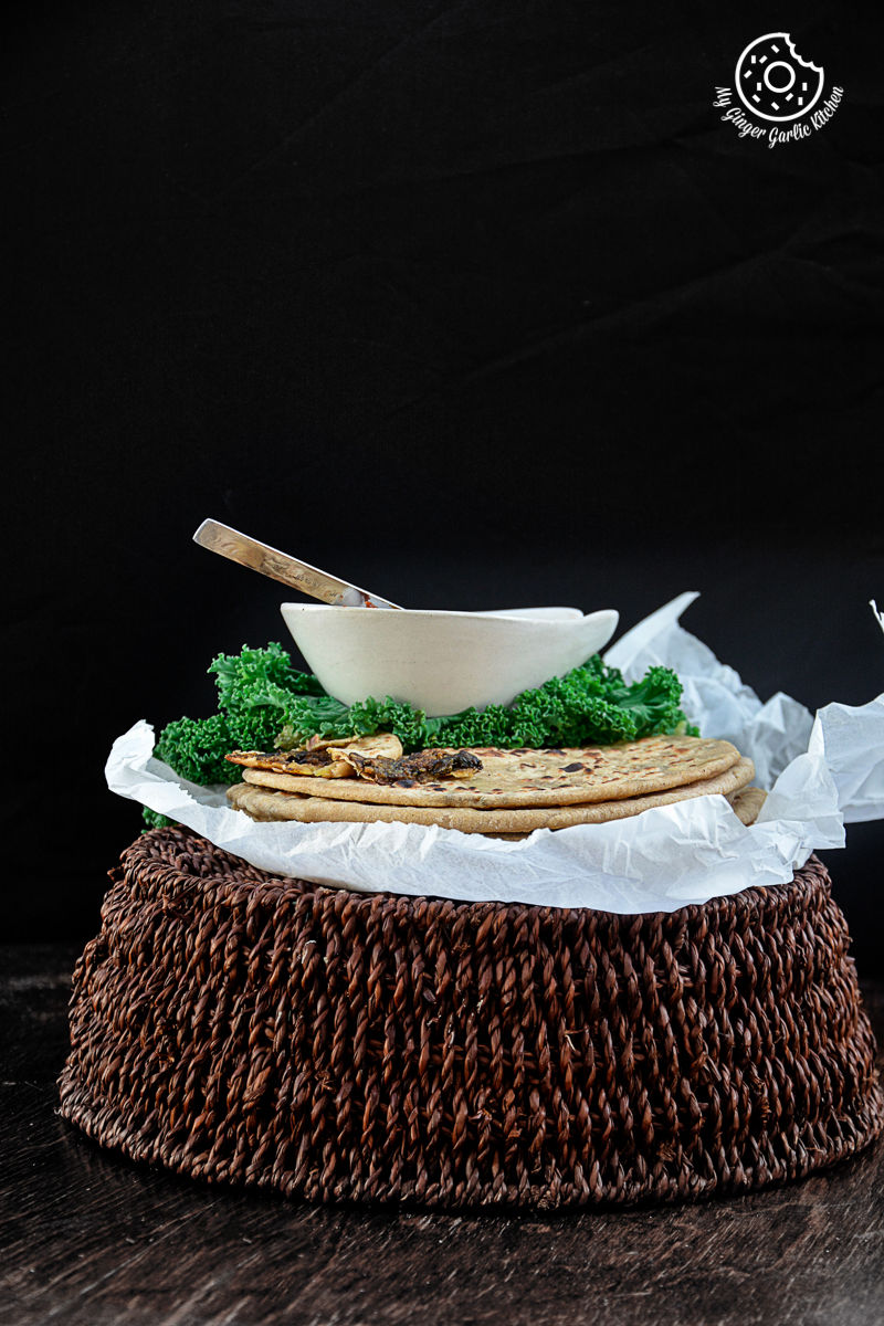 a plate mushroom kale stuffed paratha with a bowl of sauce on and kale on a basket