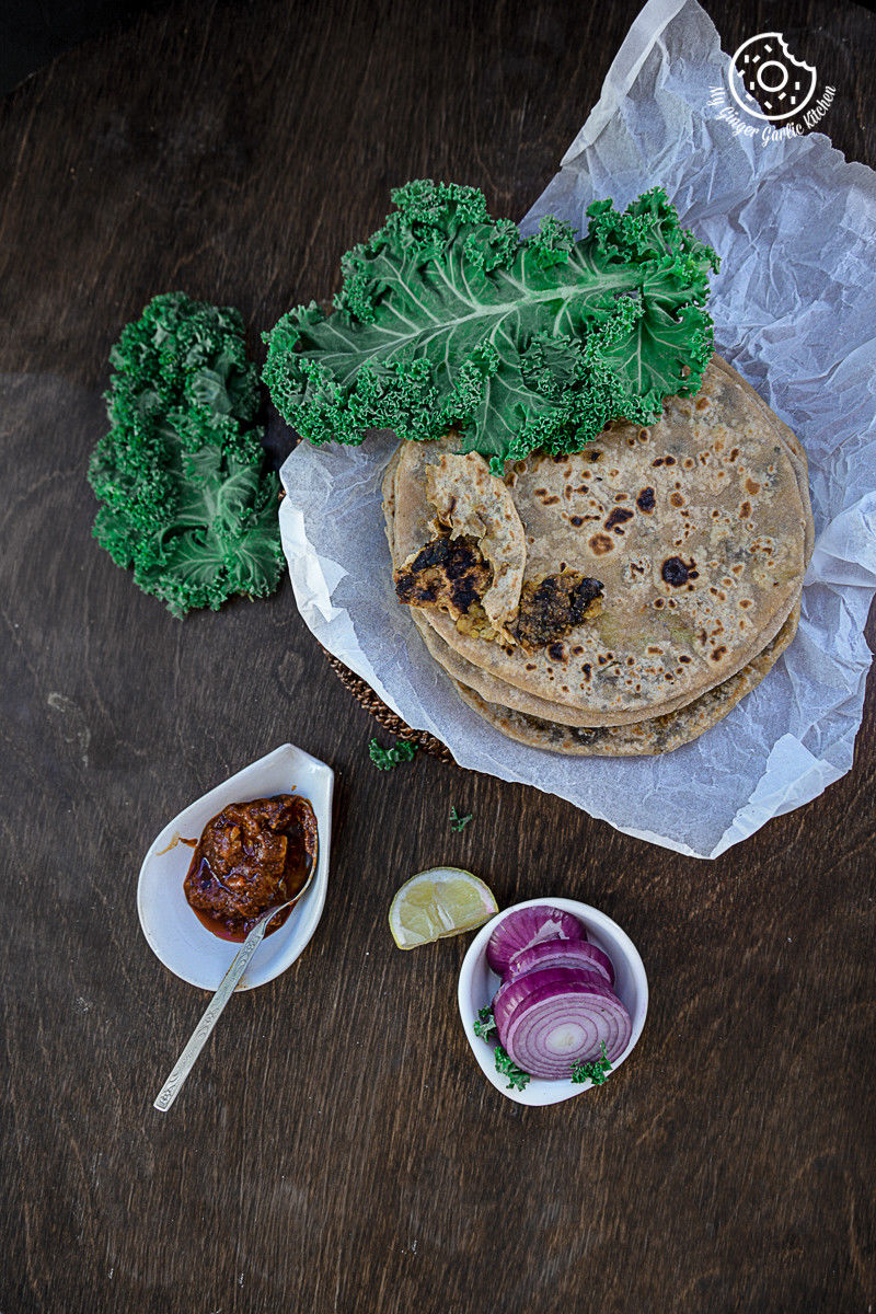 a plate of food that includes mushroom kale stuffed parathas with some pickle, onion slices and kale on the side