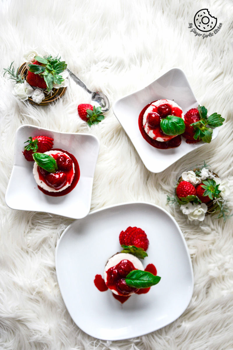 three white plates with two small white plates with no bake mini strawberry cheesecake and strawberry compote on them