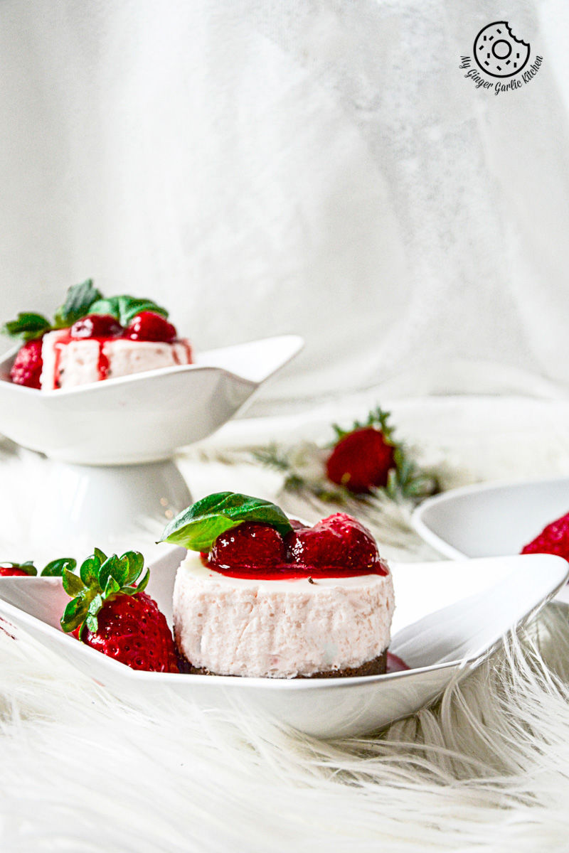 two small white plates with no bake mini strawberry cheesecake and strawberry compote on them