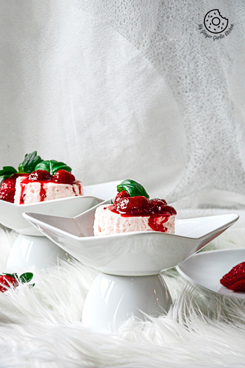 two small white plates with no bake mini strawberry cheesecake and strawberry compote on them on a white background