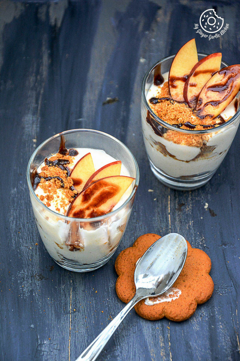 two no bake peach gingerbread cheesecake parfaits in small bowls with a spoon and cookie