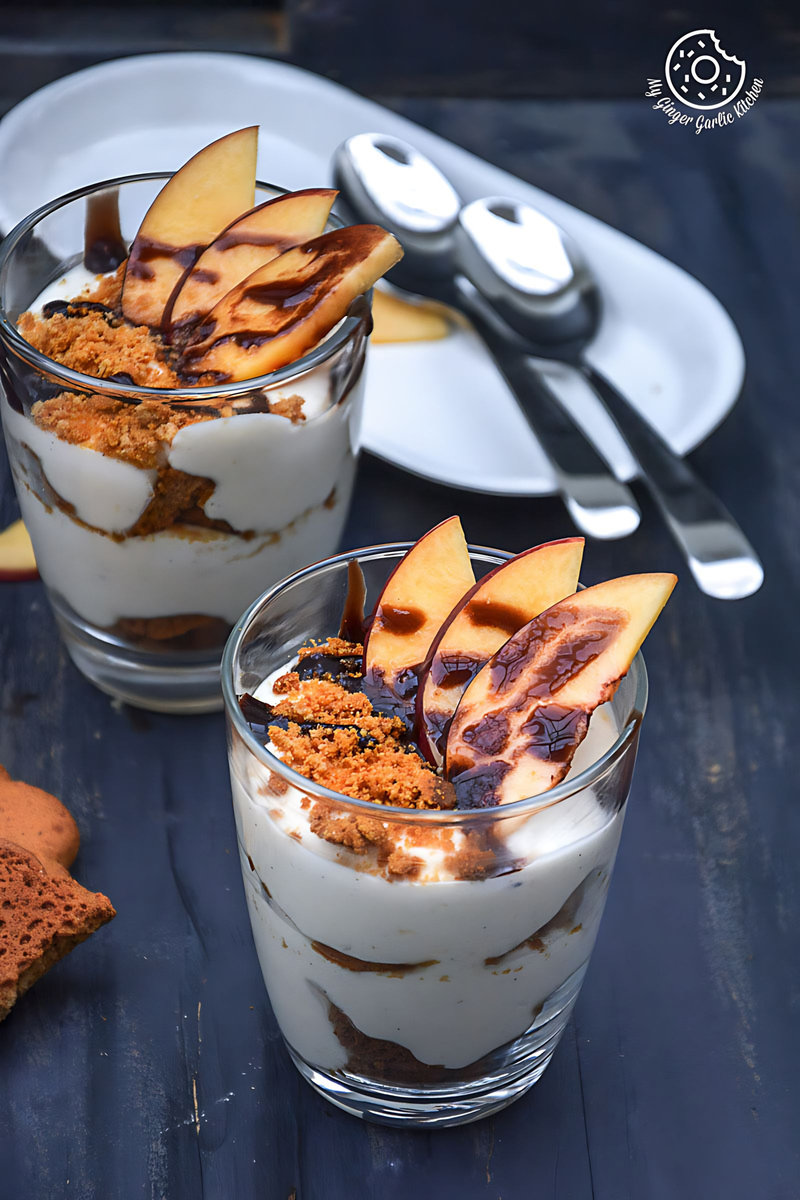 two no bake peach gingerbread cheesecake parfaits cups on a table with two spoons