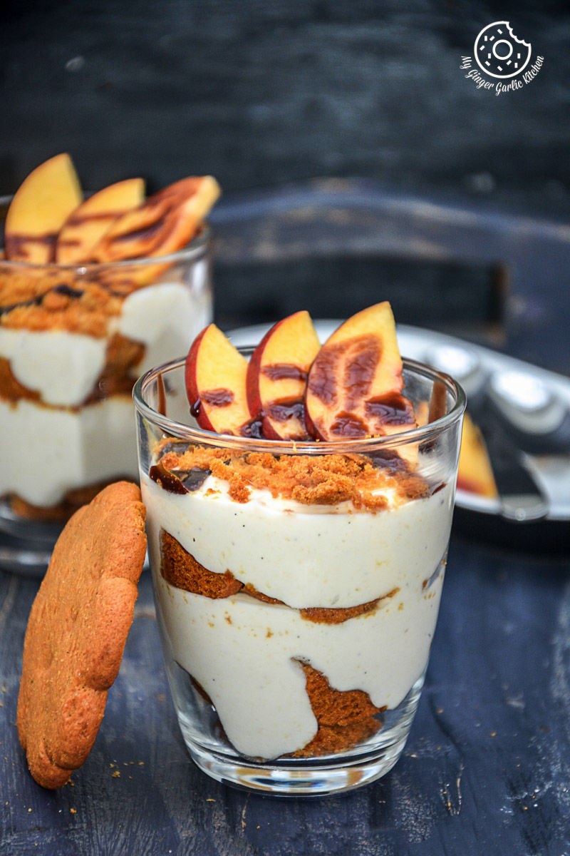 two no bake peach gingerbread cheesecake parfaits in small glasses with peaches on them