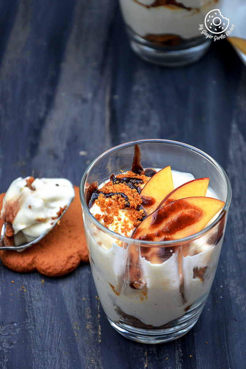 a no bake peach gingerbread cheesecake parfait in a glass with a spoon and cookie on the table