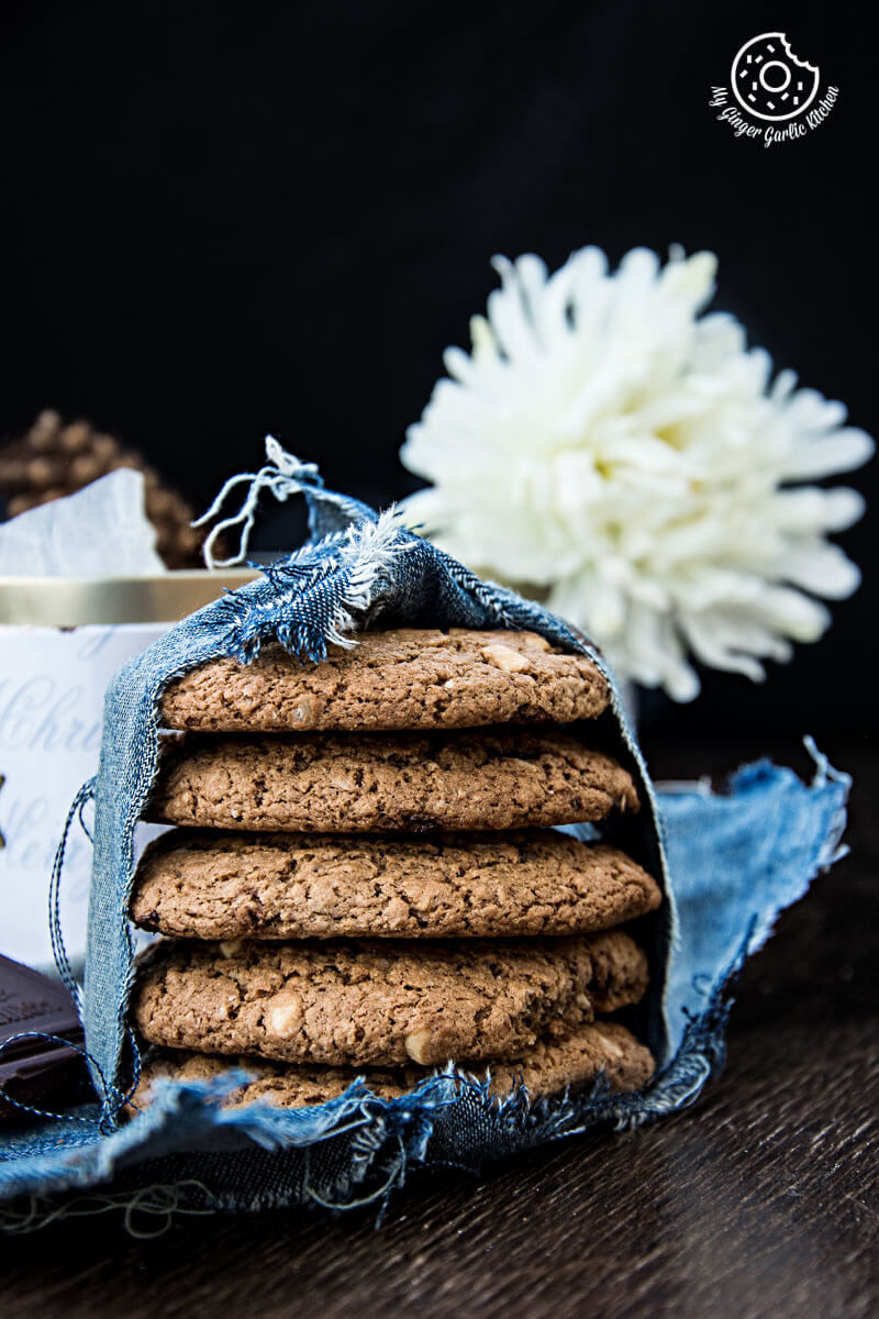 a stack of oatmeal peanut butter chocolate cookies sitting on a table with a bowl of flowers