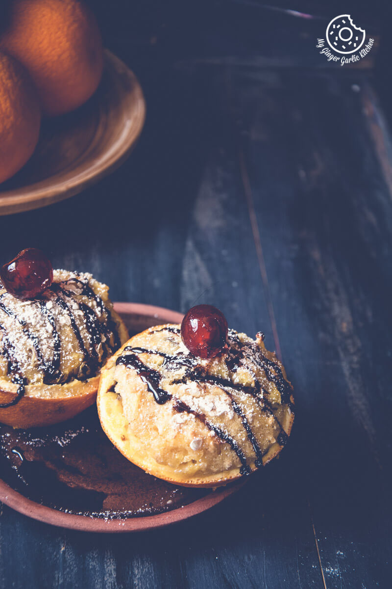 two oats orange eggless muffins on a plate with chocolate sauce and cherries
