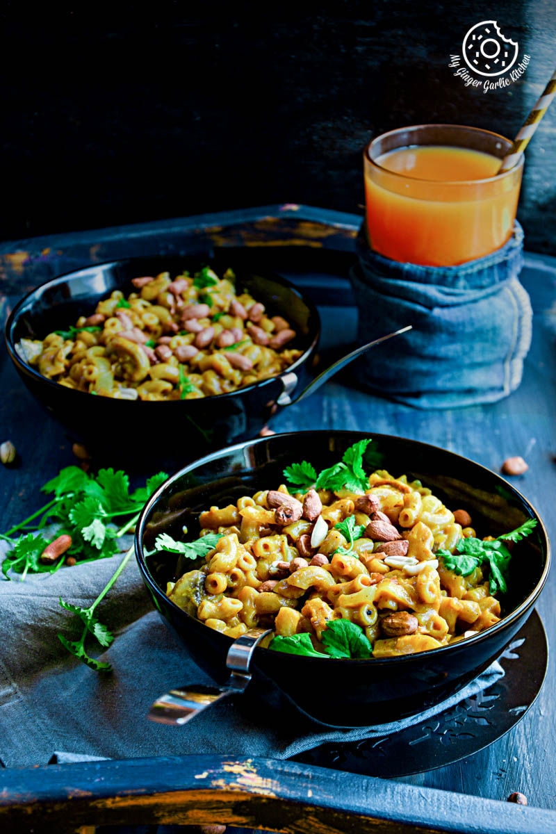 two bowls of one pan thai yellow curry macaroni on a tray with a glass of orange juice
