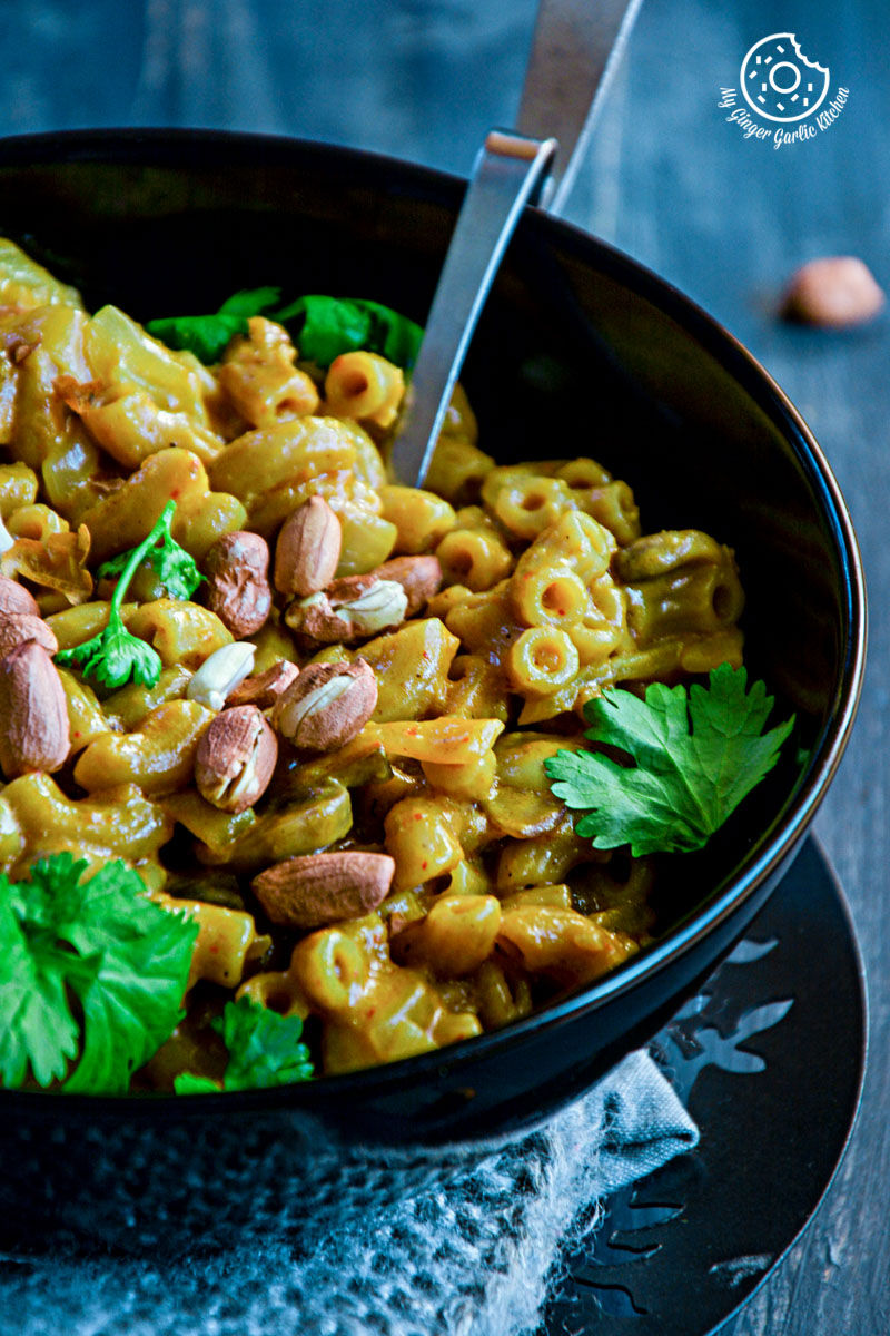 a bowl of one pan thai yellow curry mac with green leaves and peanuts in it