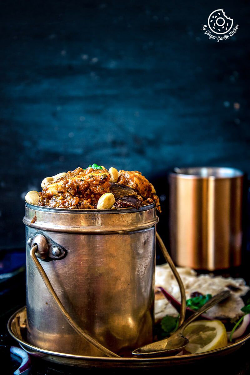 there is a metal bucket filled with Paneer Do Pyaza curry on a plate