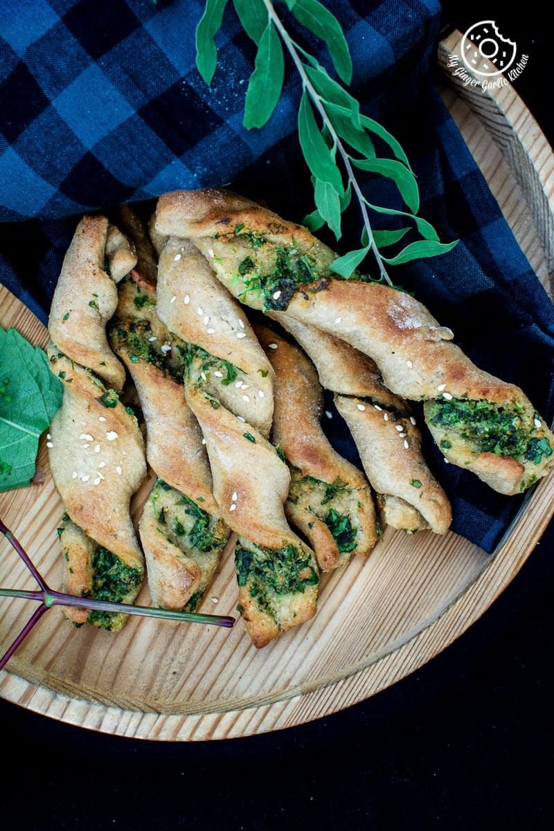 some pizza dough twists with parsley with some leaves on a wooden plate with a blue checkered cloth