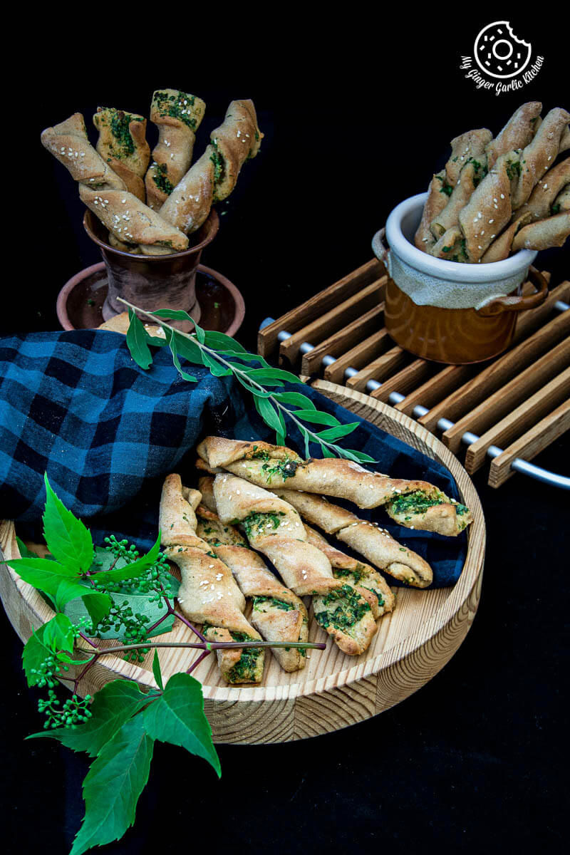 some pizza dough twists with parsley with some leaves on a wooden plate