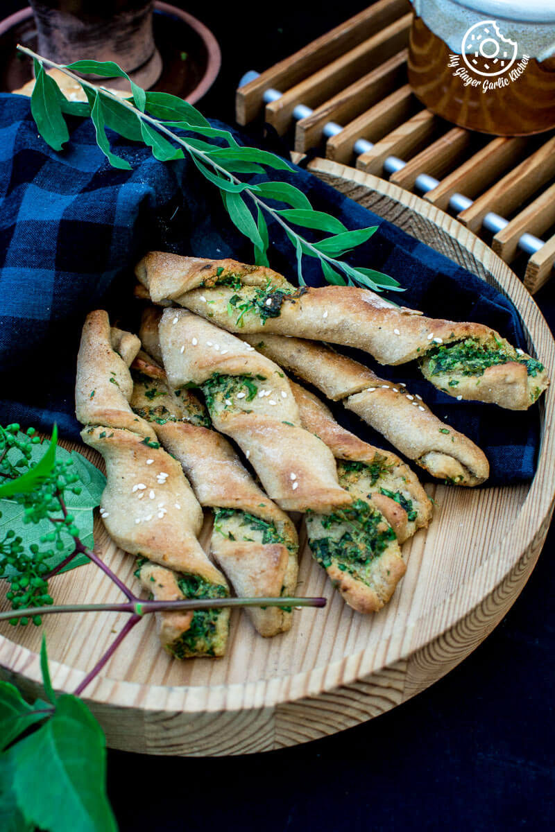 pizza dough twists with parsley with some leaves on a wooden plate with a blue cloth