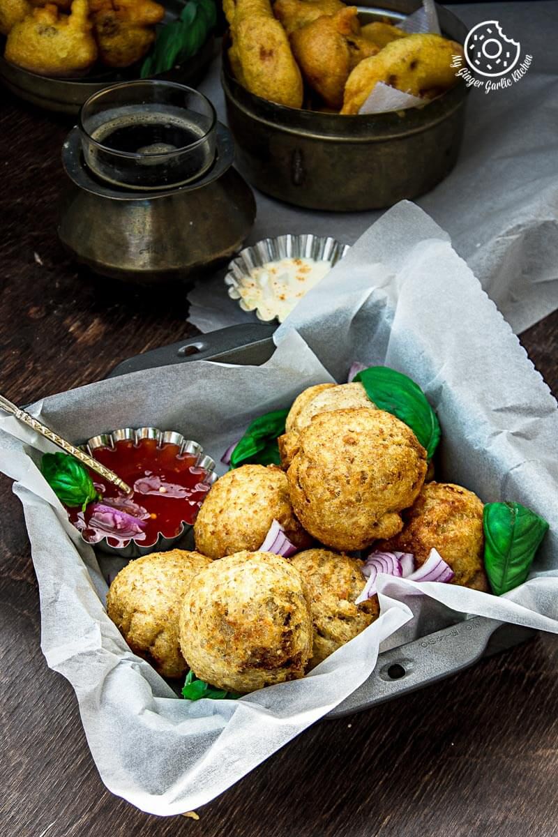 a basket of fried potato stuffed bread rolls on a table with a bowl of sauce