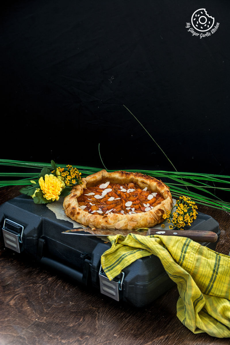 a puff pastry apricot galette with almond topping on a piece of luggage with flowers