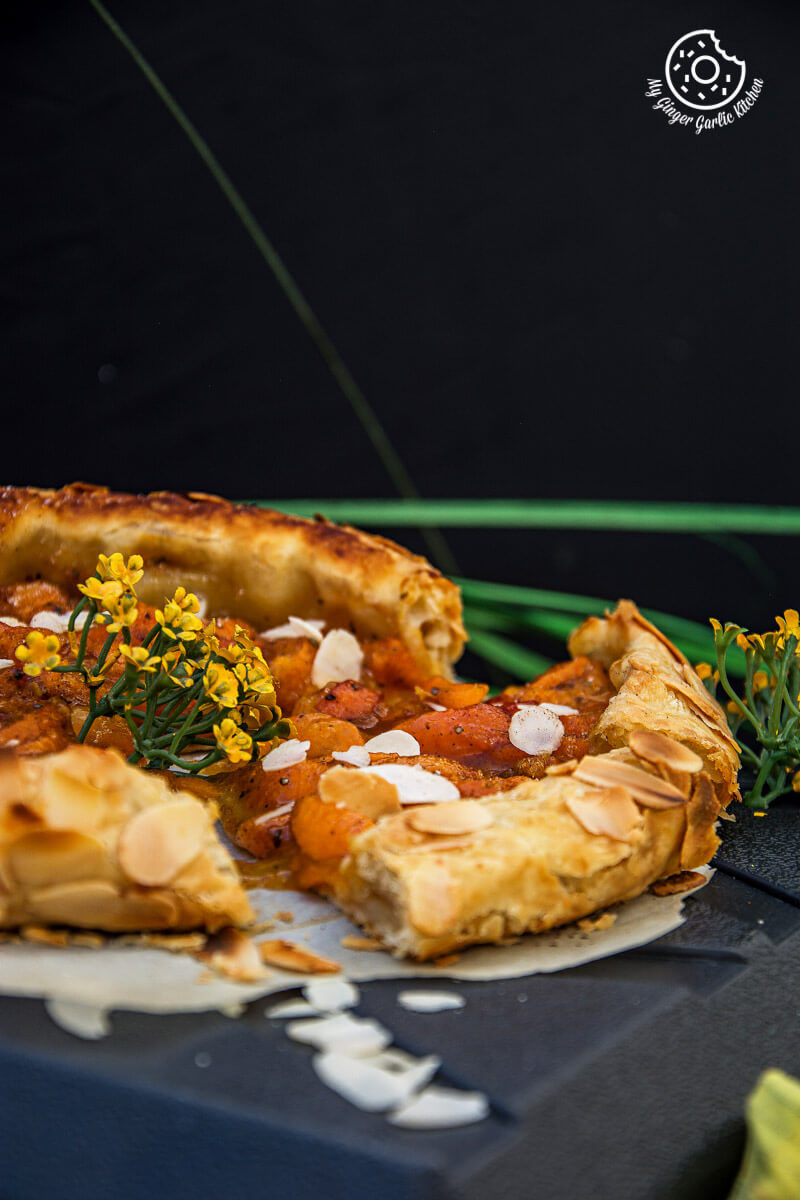 a puff pastry apricot galette with almond topping with a slice missing from it on a table