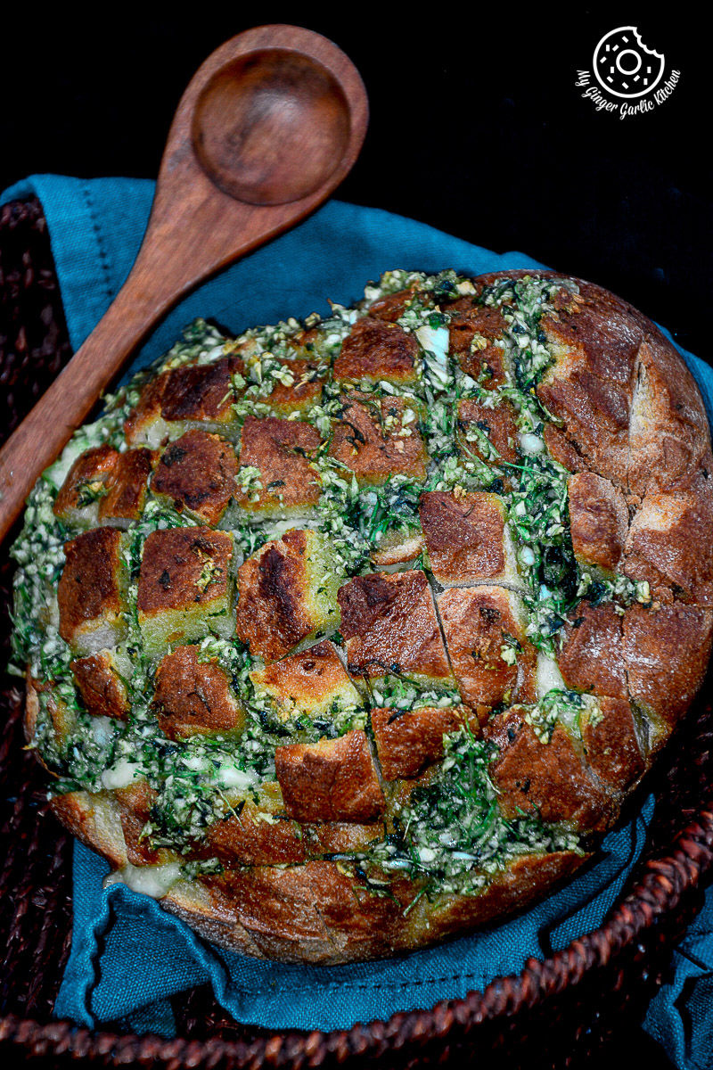a pull apart garlic parsley bread with a wooden spoon on a blue cloth