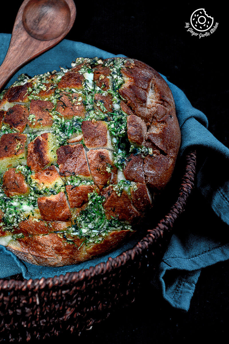 a pull apart garlic parsley bread with a wooden spoon in a basket