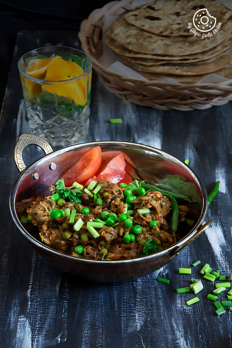 there is a bowl of Punjabi Baingan Bharta with vegetables and a glass of water