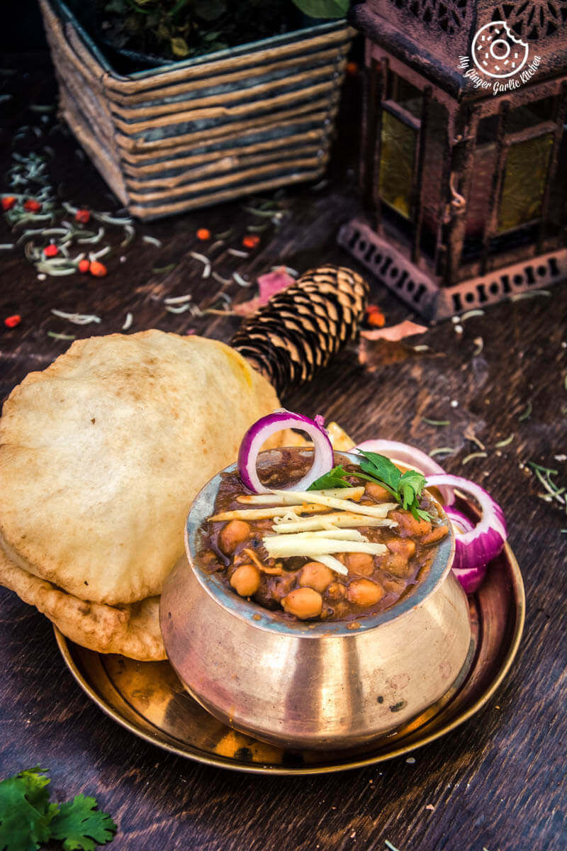 there is a bowl of chole topped ginger, onion with some bhature and a pine cone