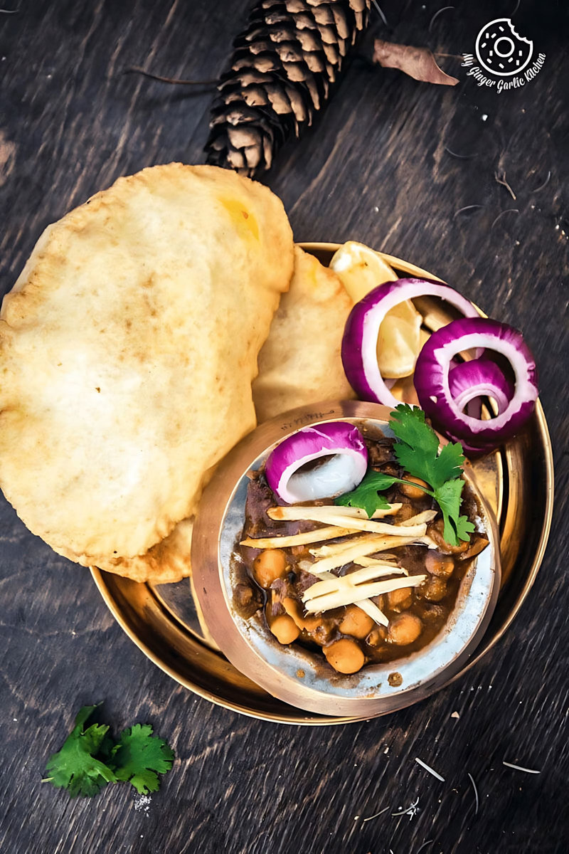 there is a bowl of chole bhature with cilantro and pine cone on the side