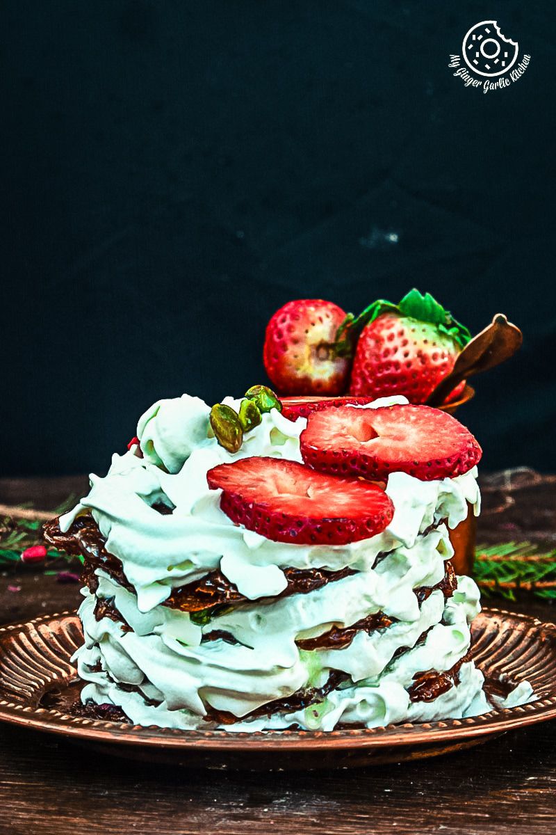 a stack of rajasthani mawa malpuas topped with whipped cream with strawberry on a plate