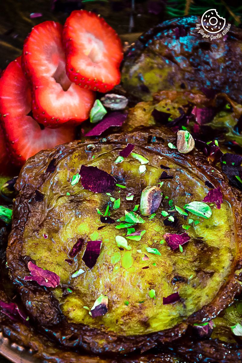 a plate of rajasthani mawa malpua topped with a pistachios and strawberries on it