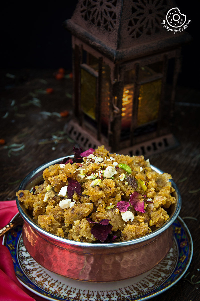 a bowl of rajasthani moong dal halwa garnished with nuts on a plate with a lantern in the background