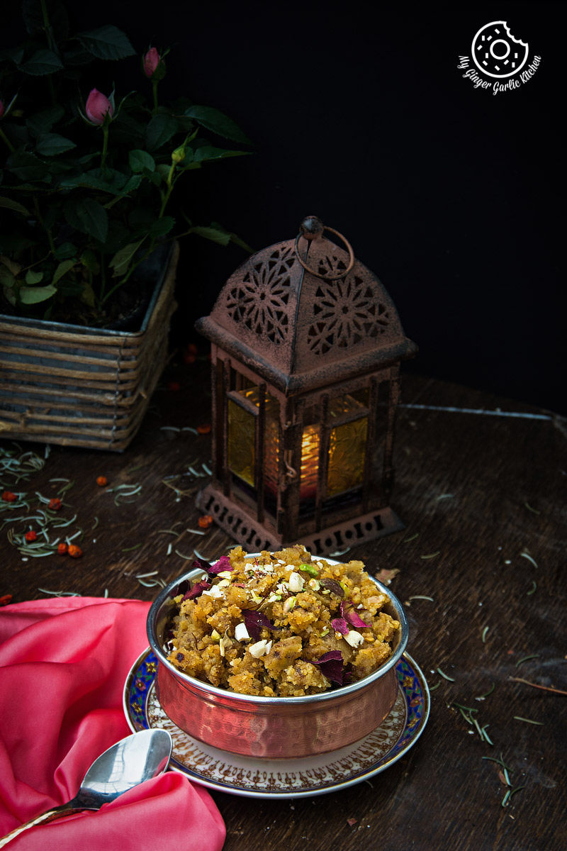 a plate of rajasthani moong dal halwa garnished with nuts on a table with a lantern