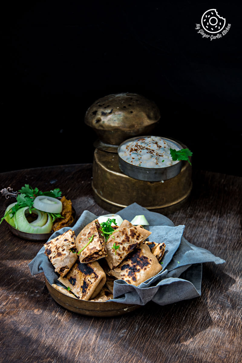 a plate of rajma tofu pocket paratha bites with boondi raita, with pickle and onion slices on a table