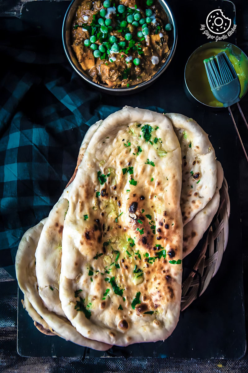 a stack of Restaurant Style Indian Garlic Naan with a ghee bowl on the side with a bowl of curry