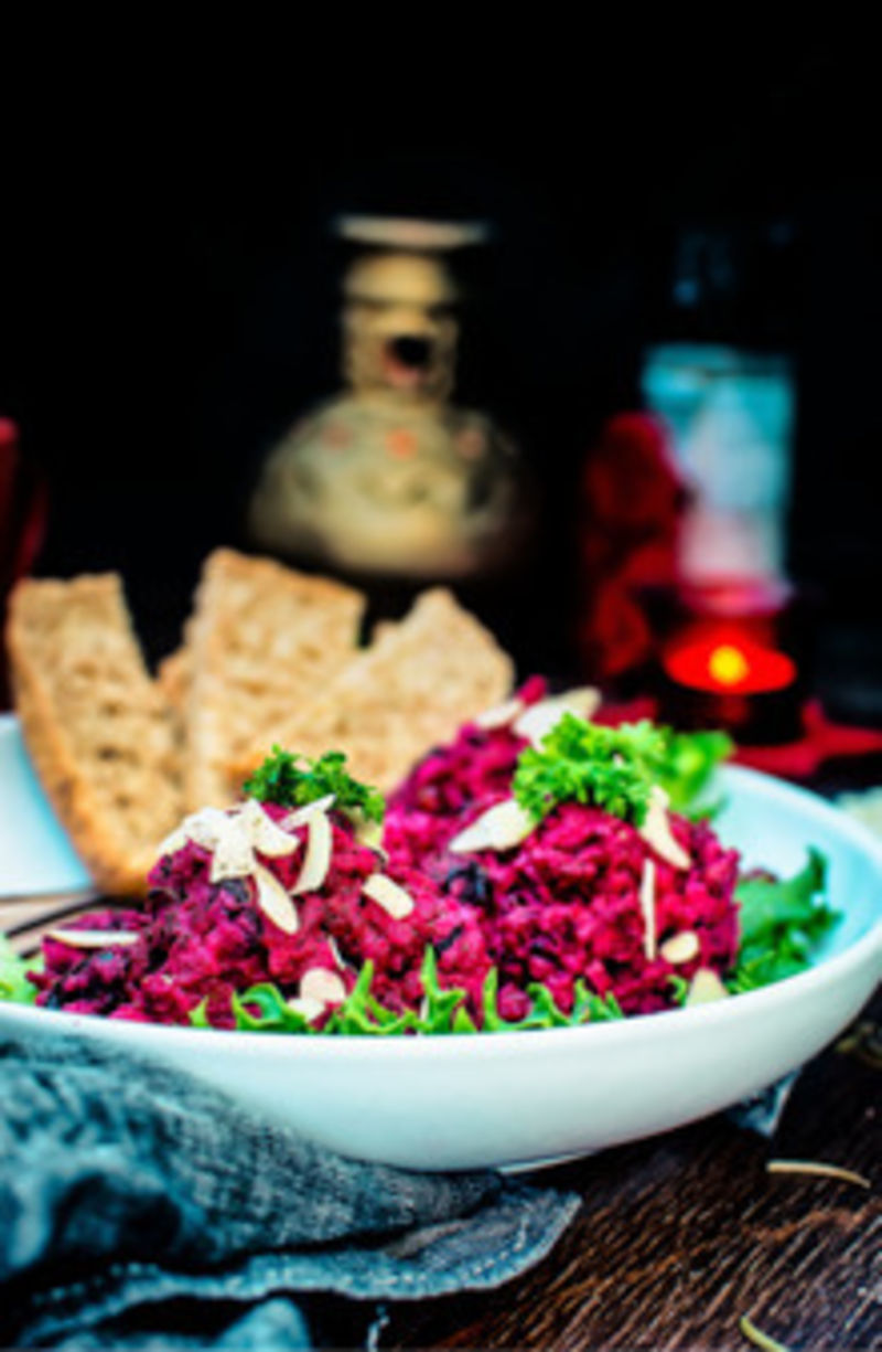 a bowl of roasted beet potato holiday salad with a candle in background