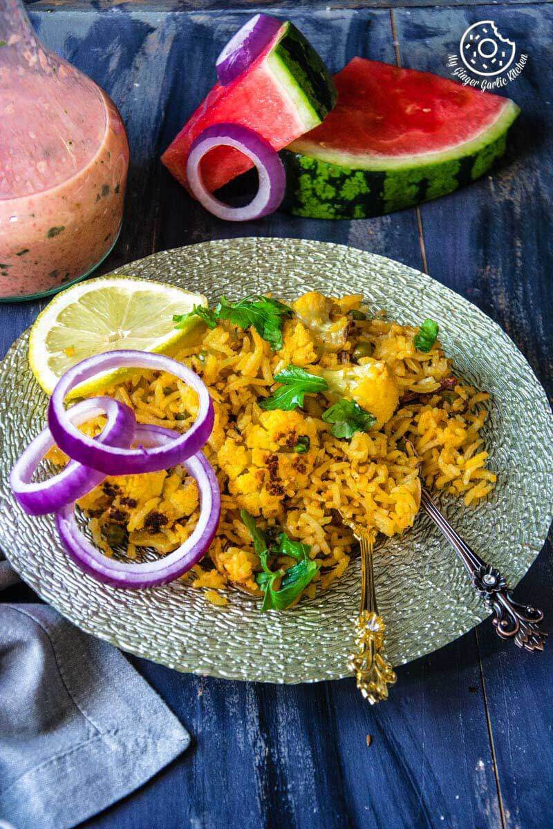 a plate of roasted cauliflower pulao with onions on it and watermelon sauce on the side
