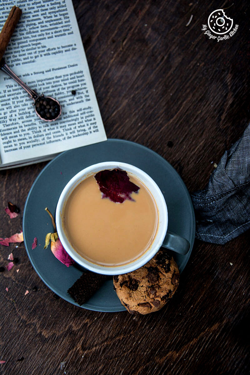 a cup of rose masala chai and a chocolate chip cookie on a table with a book