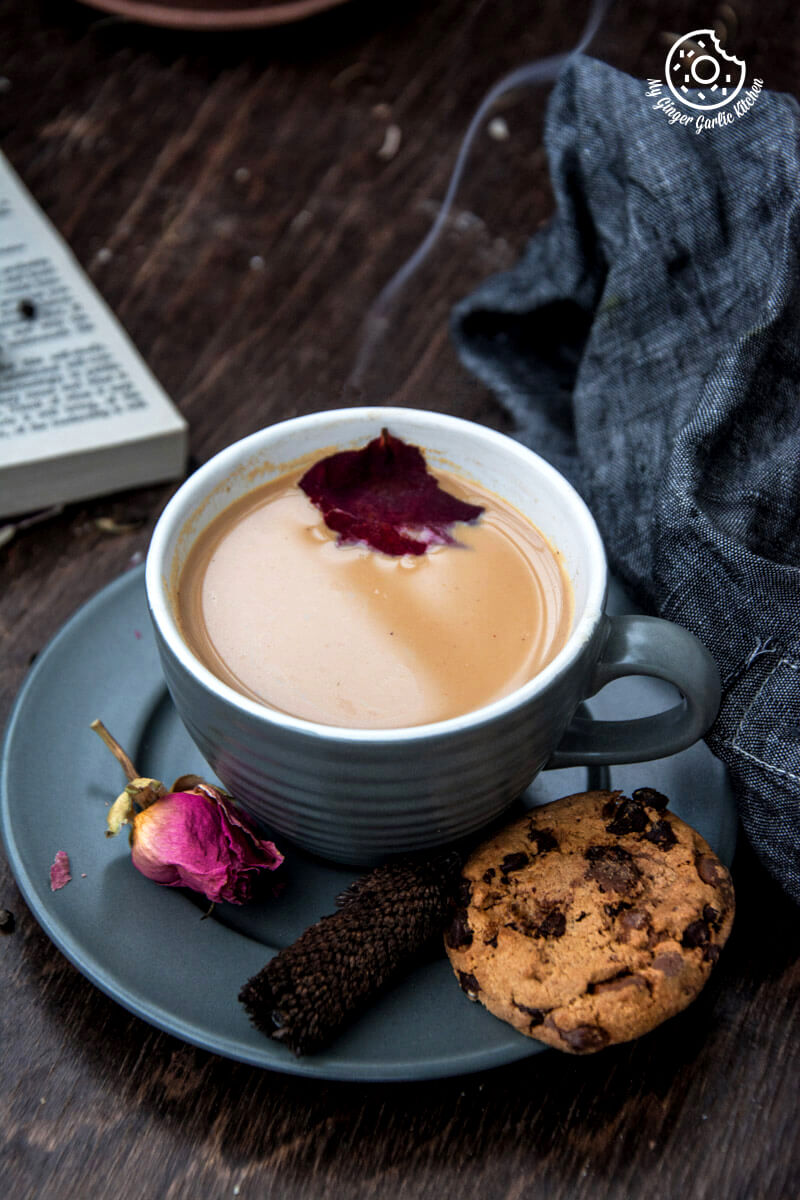 a cup of rose masala chai and a chocolate chip cookie on a table with a table cloth