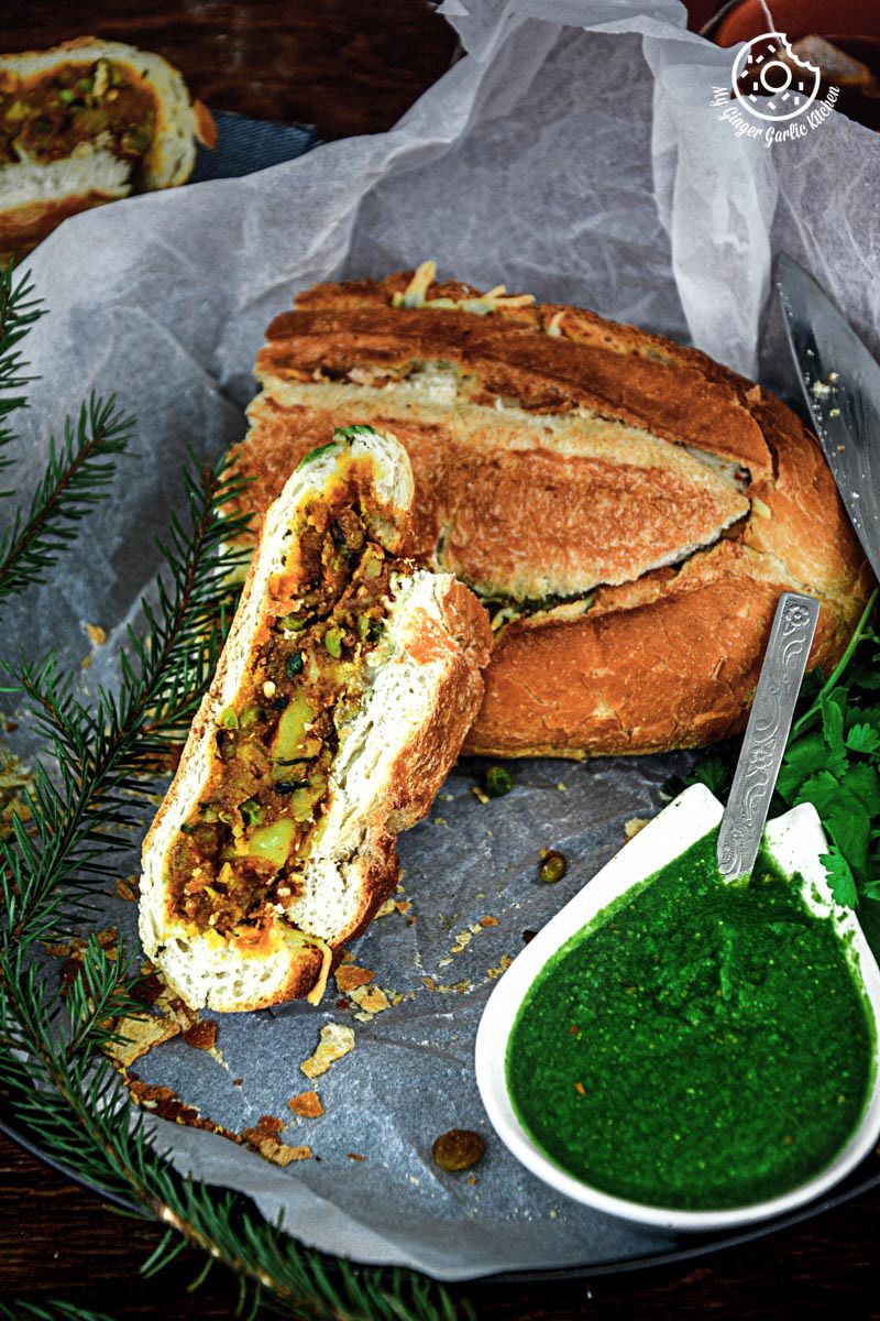 a samosa french loaf with a side of green coriander chutney on a plate