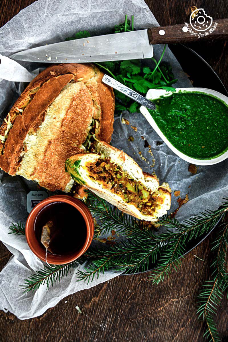 a samosa french loaf with a slice of it on a plate with a bowl of green sauce