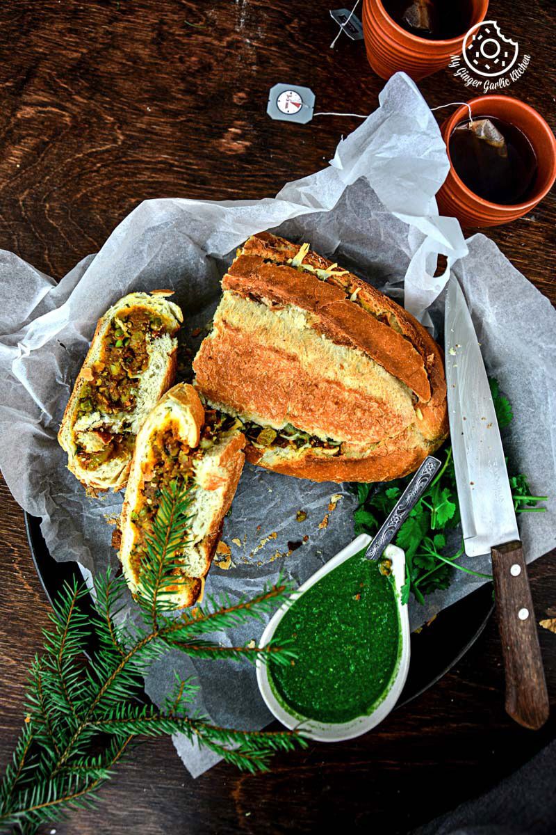 a samosa french loaf on a plate with a knife and a bowl of coriander chutney