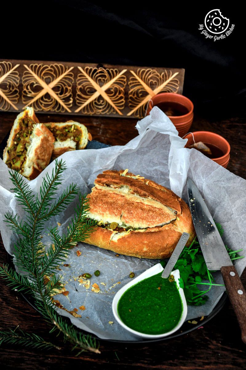 a samosa french loaf on a plate with a knife and a bowl of green coriander chutney